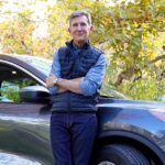 Man reviewing Hartford car insurance savings options next to his blue car.