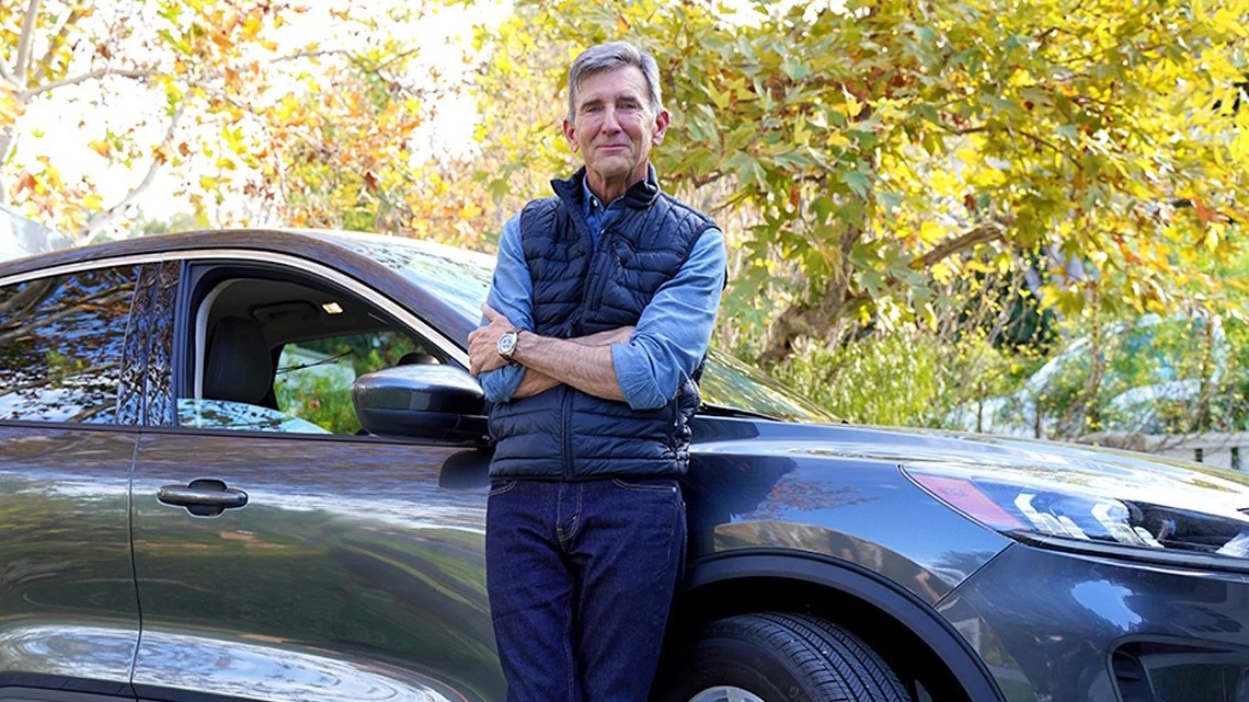 Man reviewing Hartford car insurance savings options next to his blue car.