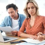 Couple smiling and looking at a tablet, considering auto loan refinance options with a refinance car loan calculator for better financial planning.