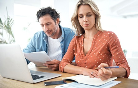 Couple smiling and looking at a tablet, considering auto loan refinance options with a refinance car loan calculator for better financial planning.