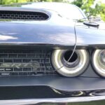 Front three quarter view of the Dodge Challenger Black Ghost parked on a city street at dusk, showcasing its aggressive stance and unique black and white styling.