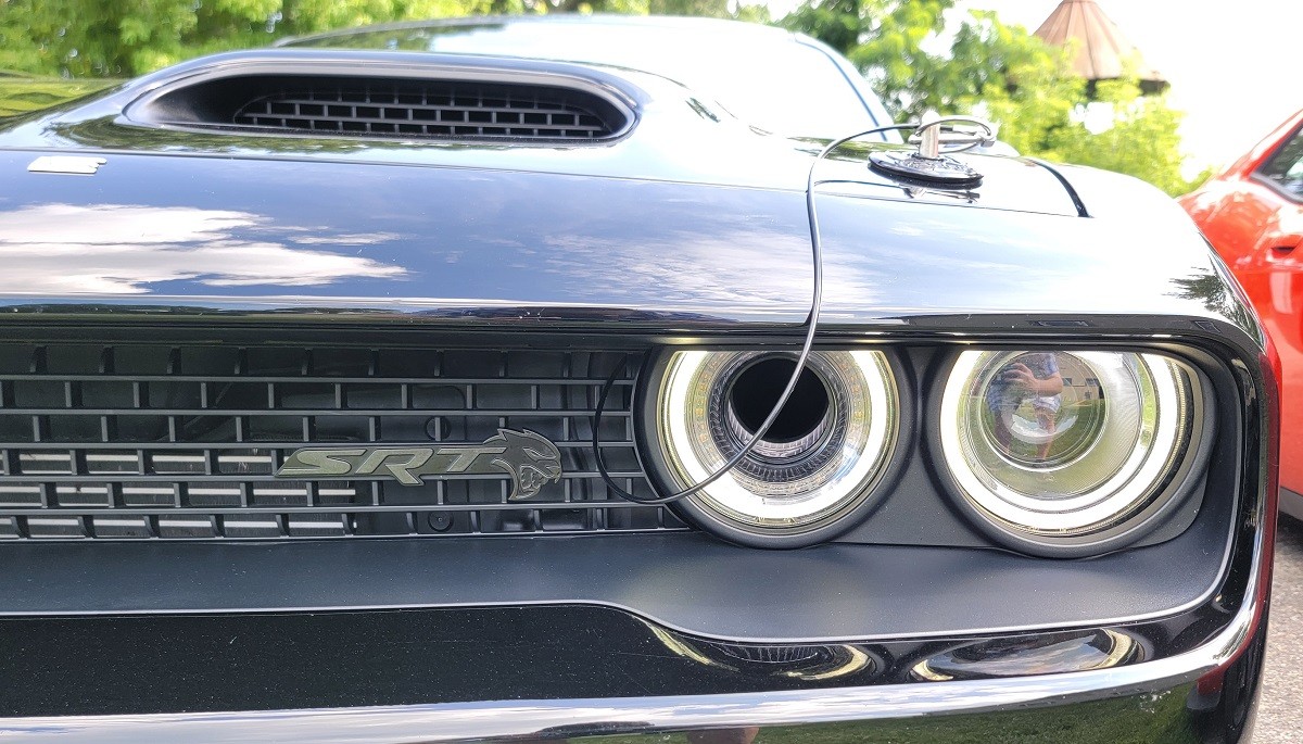 Front three quarter view of the Dodge Challenger Black Ghost parked on a city street at dusk, showcasing its aggressive stance and unique black and white styling.