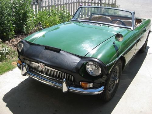 Close-up of a car bra (front vest) being fitted onto a classic MG car, showing the strap and wheel well area, highlighting car bra installation