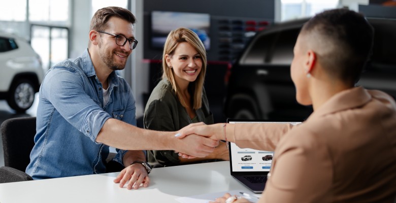 A car buyer shakes hands with a dealer after securing financing, illustrating the common scenario where a car lien is established to protect the lender's investment.