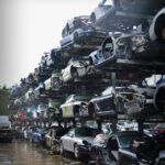 Vertical racks filled with luxury cars at a UK car scrap yard, showcasing Porsches and other high-end vehicles.