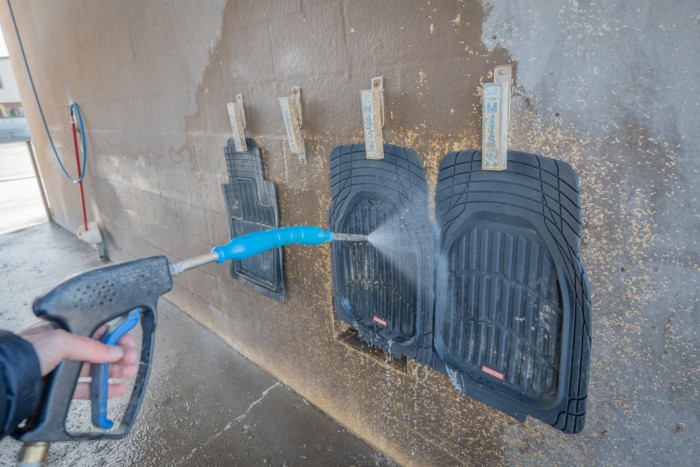 Person spraying down car floor mats at a car wash for cleaning