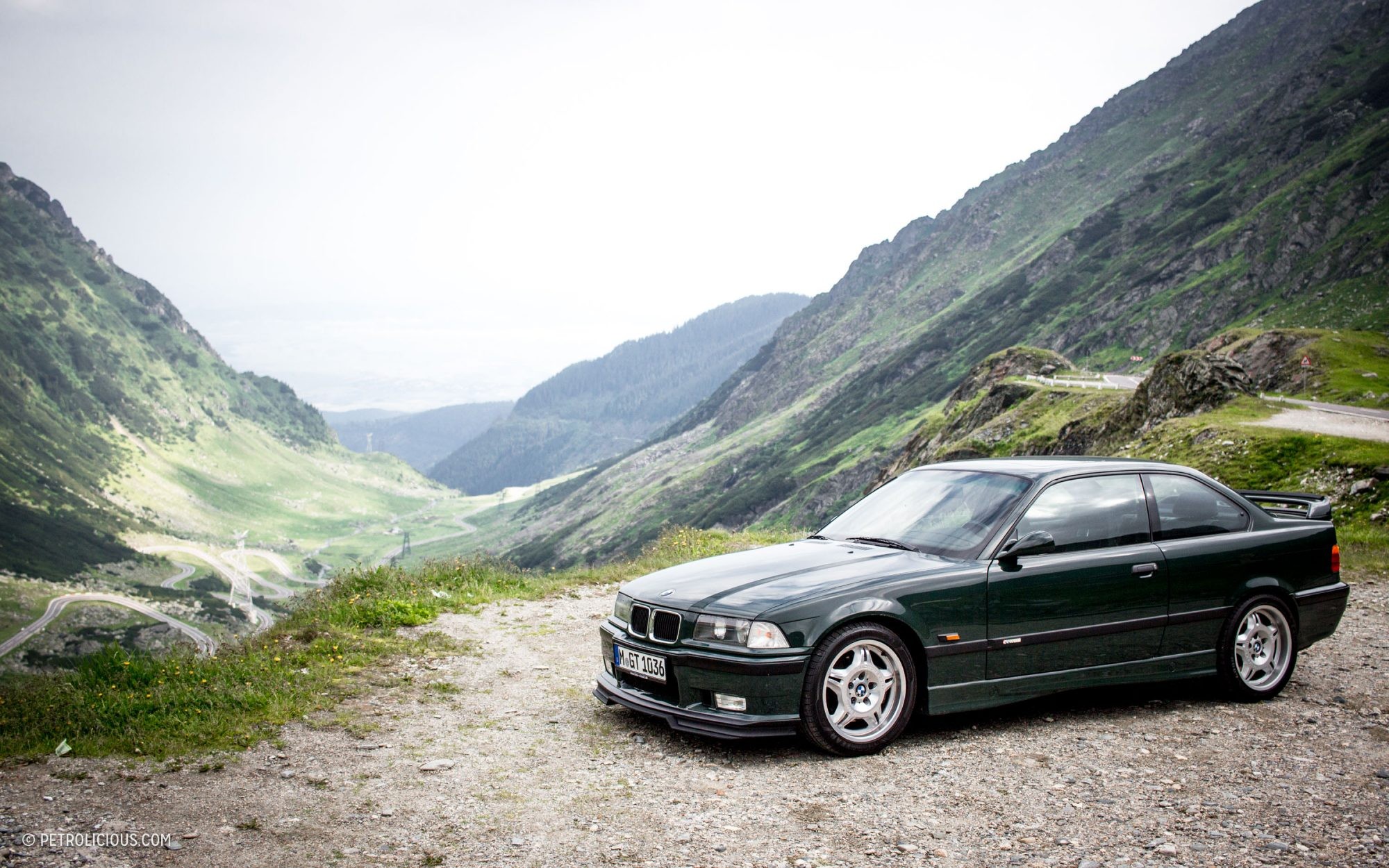 British Racing Green BMW E36 M3 GT parked on a scenic road, showcasing its sporty profile and rear wing