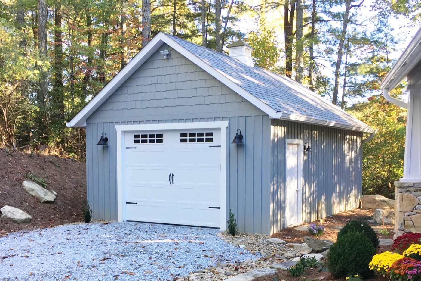 Prefab single car garage with white siding and green doors.