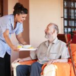 Elderly Senior Being Brought Meal By Carer Or Nurse