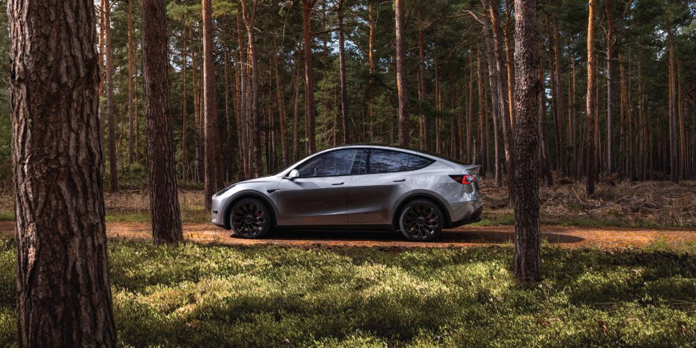 Tesla Model Y cinza dirigindo por uma estrada na floresta.